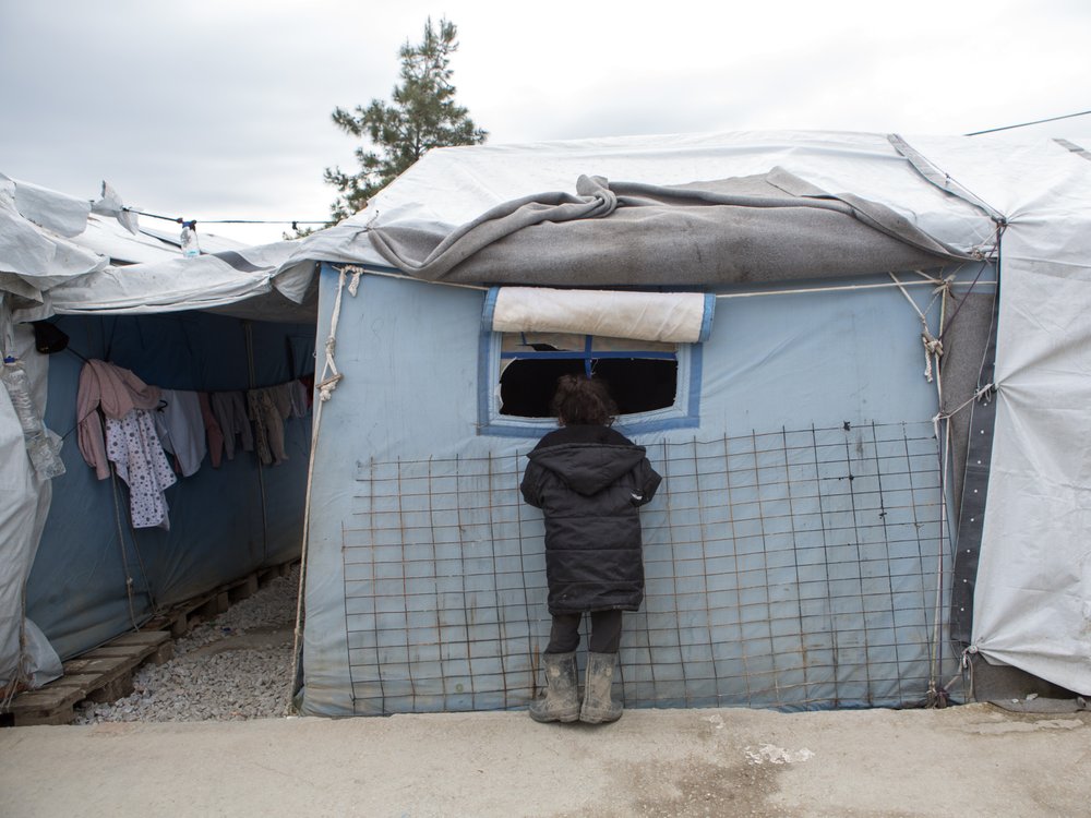 A child looks through the window of a shelter in Moria camp, Lesbos